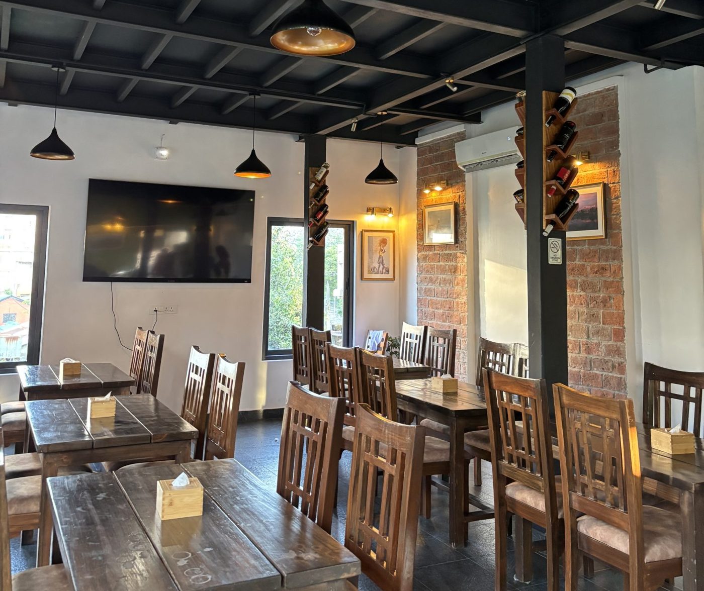 Dining room with heavy wooden tables and chairs, a brick wall and dark steel beams overhead