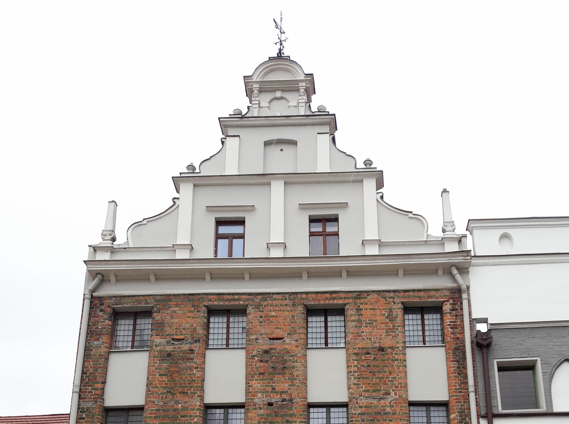 Gothic brick granary front in Toruń, tall windows between brick piers under a white rendered gable