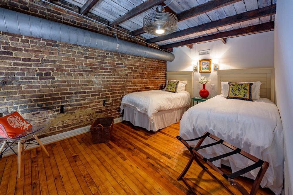Hotel room with a bare brick wall, a plank ceiling with a dark timber beam and a wide oak floor